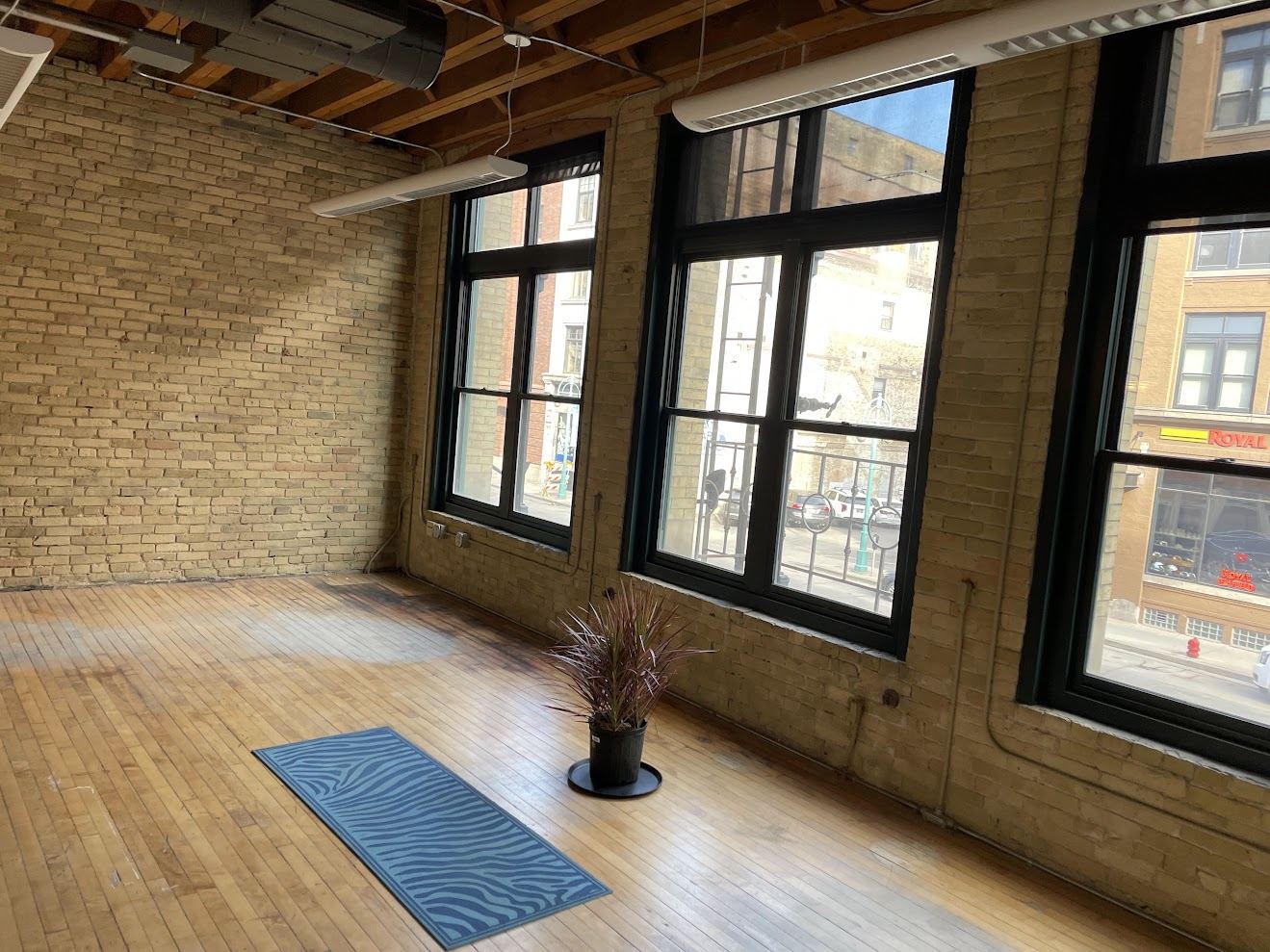 Corner of Suite 200 with exposed Cream City brick walls, original maple floor, and tall dark-framed windows looking onto Water Street.