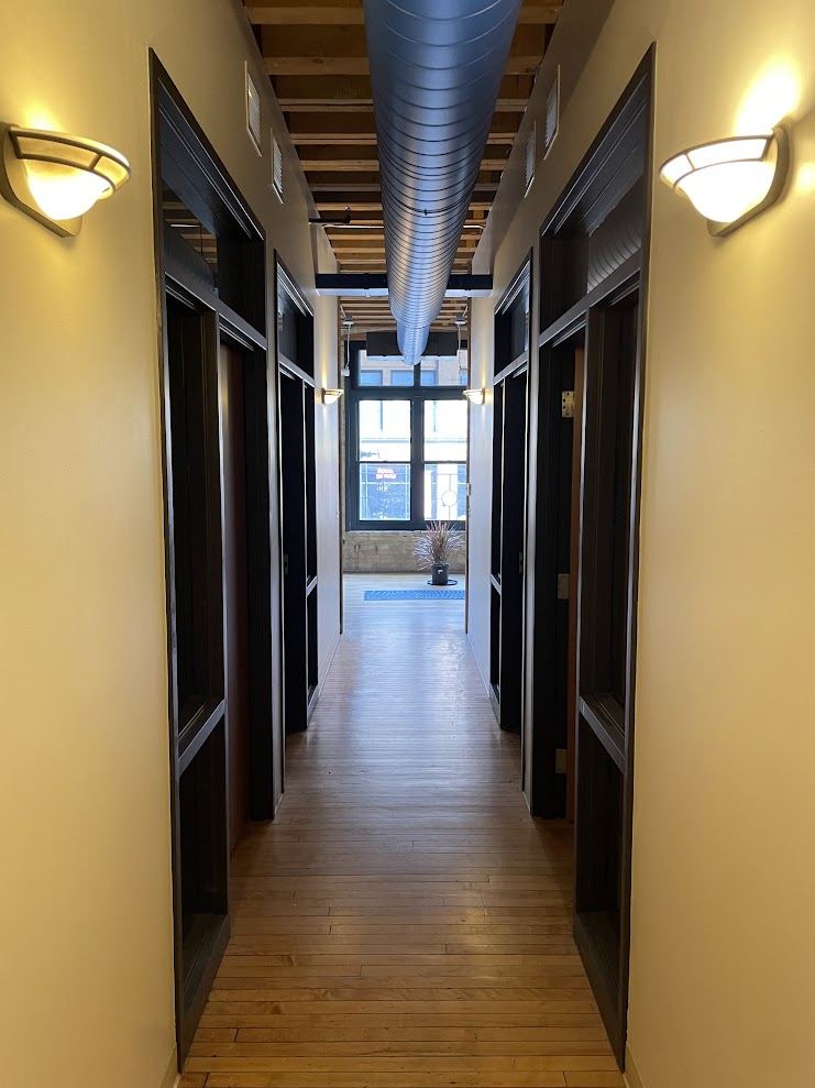 Central corridor in Suite 200 lined with private office doors, timber ceiling overhead and daylight at the far end.