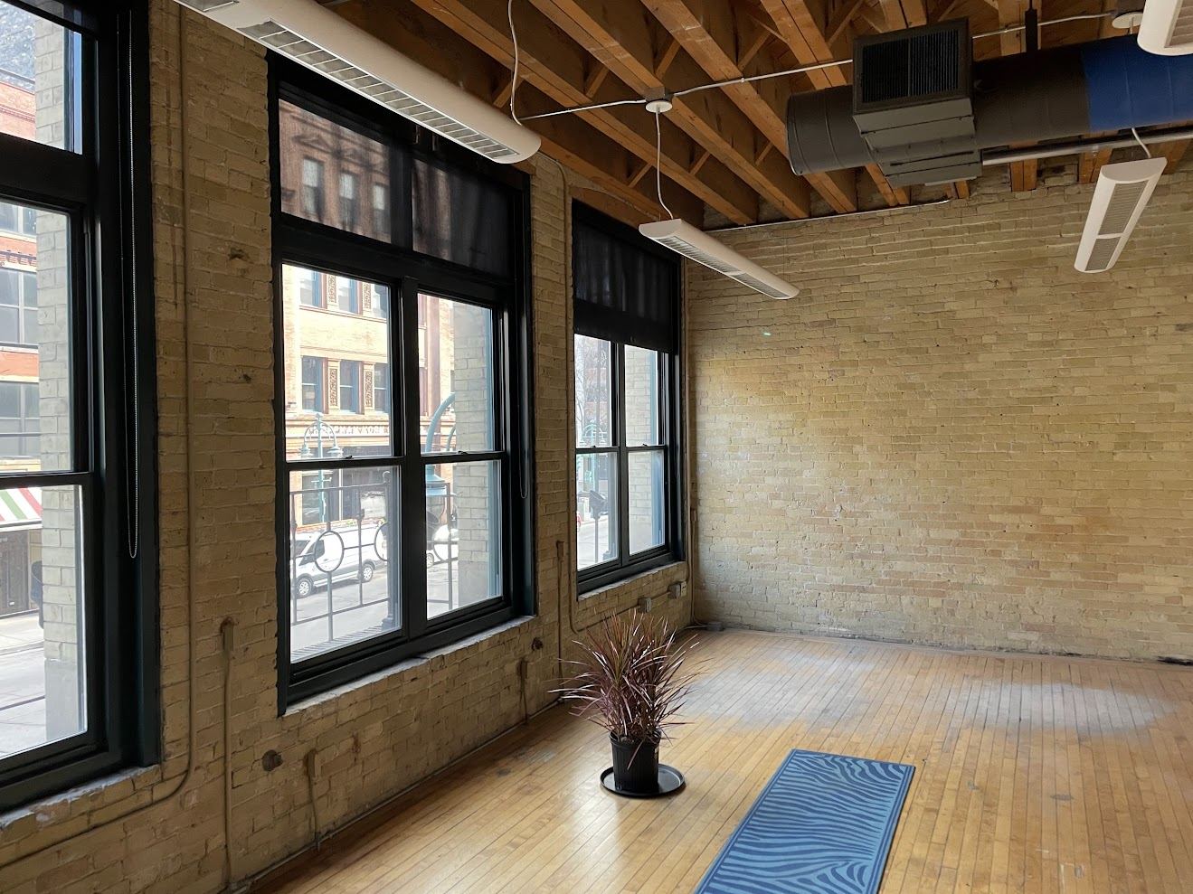 Open area of Suite 200 with brick wall, timber ceiling and a row of windows facing Water Street.