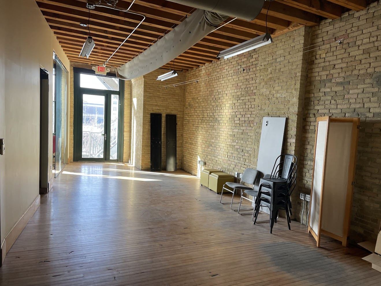 Long open area in Suite 250 with a full-height Cream City brick wall, exposed timber joists and a door to the river landing at the far end.