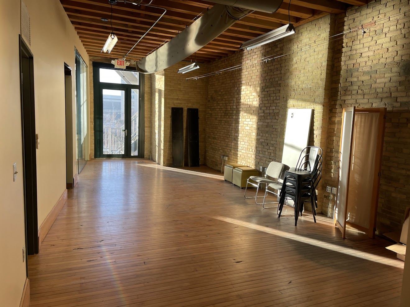 Wide view of Suite 250's open area with brick on one side, private office doors on the other and daylight from the river end.