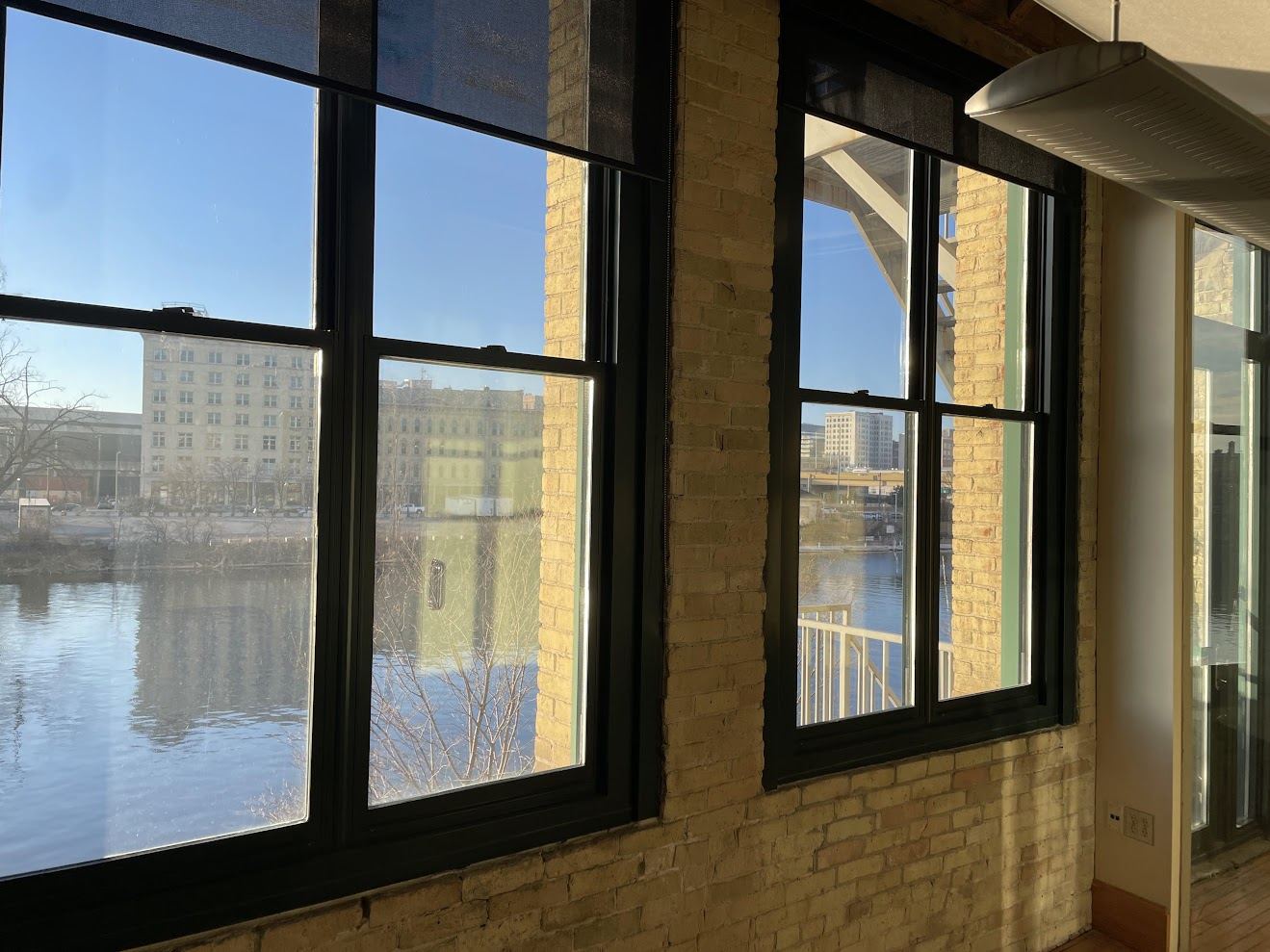 Tall river-facing windows in Suite 250 set between Cream City brick piers, looking across the Milwaukee River toward downtown.