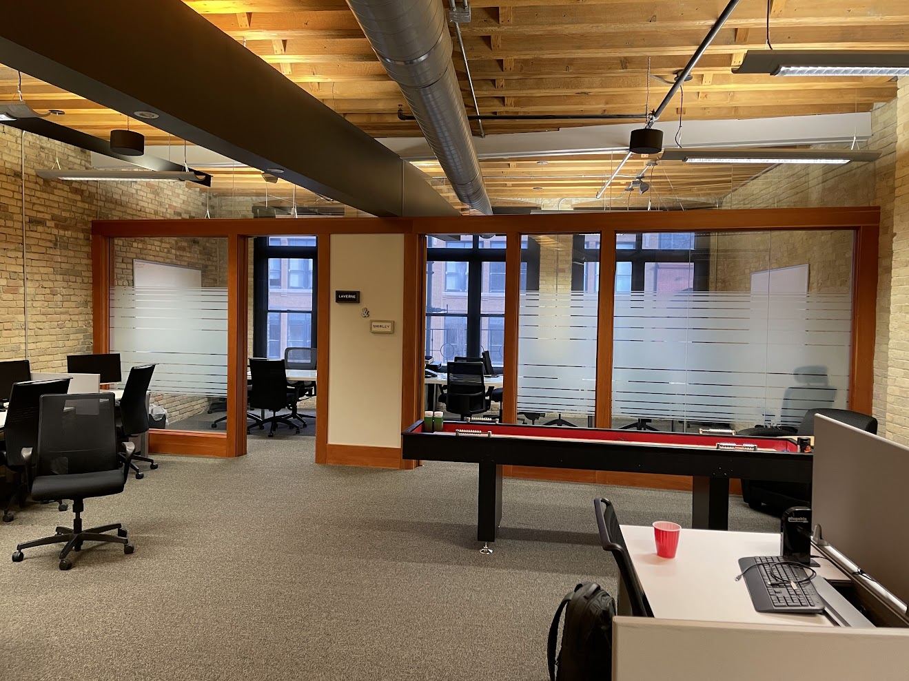 Suite 400 looking toward two glazed meeting rooms framed in wood, with exposed brick and timber ceiling in the open area beyond.