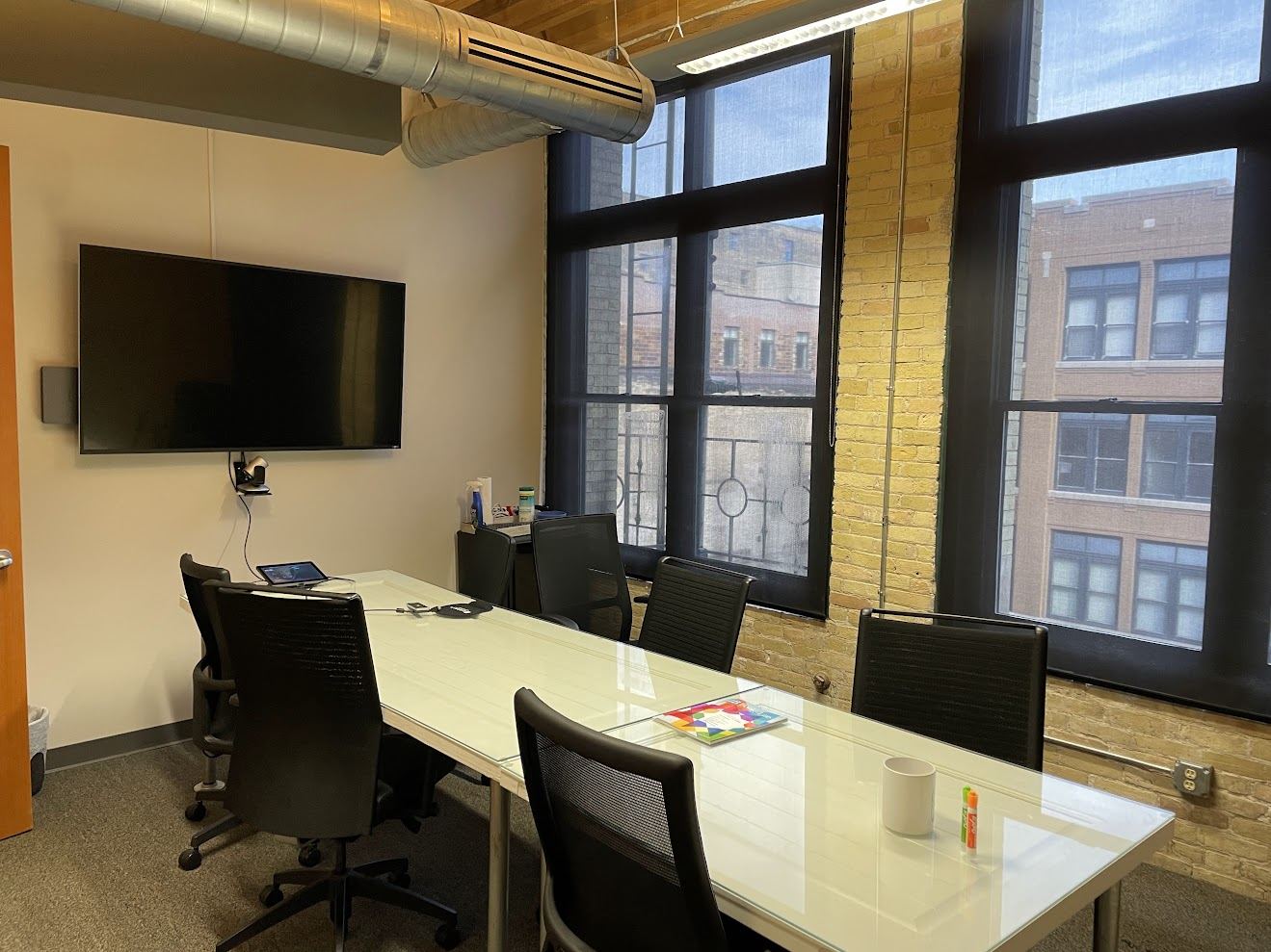 Street-facing meeting room in Suite 400 with a wall-mounted display and two tall windows between brick piers.