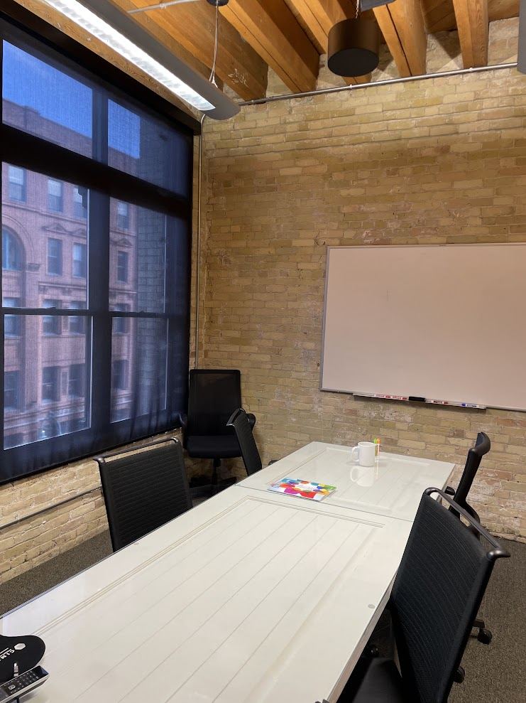 Meeting room in Suite 400 with brick walls, a whiteboard and a tall window looking across Water Street.